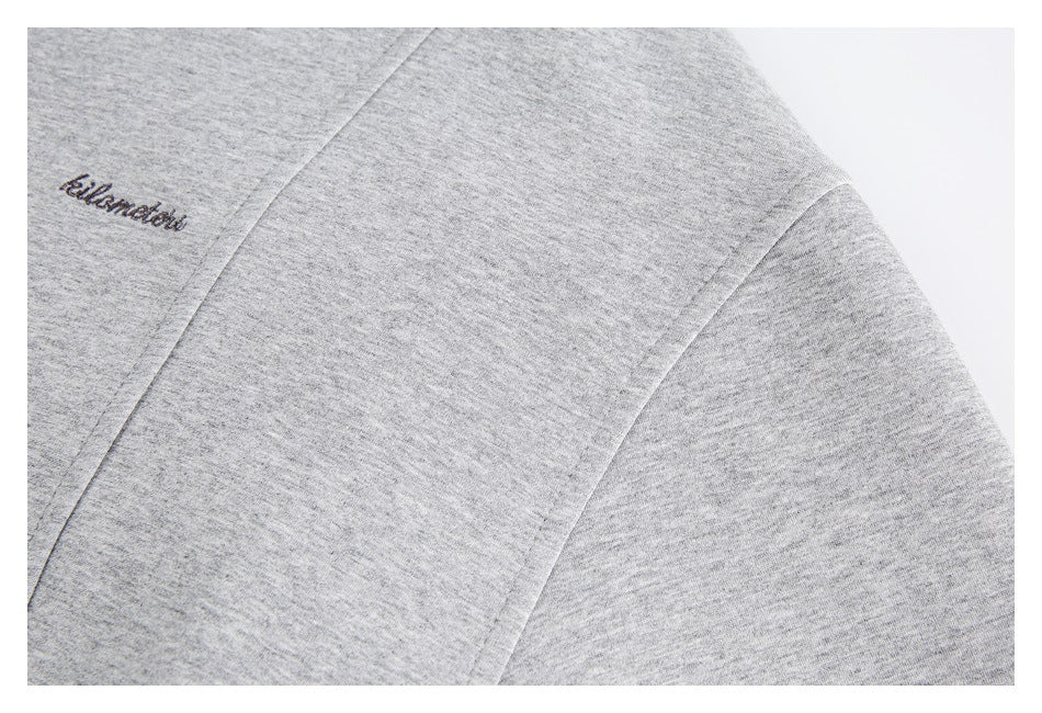 Close-up of heather-gray fabric with curved seams and small dark cursive embroidery.
