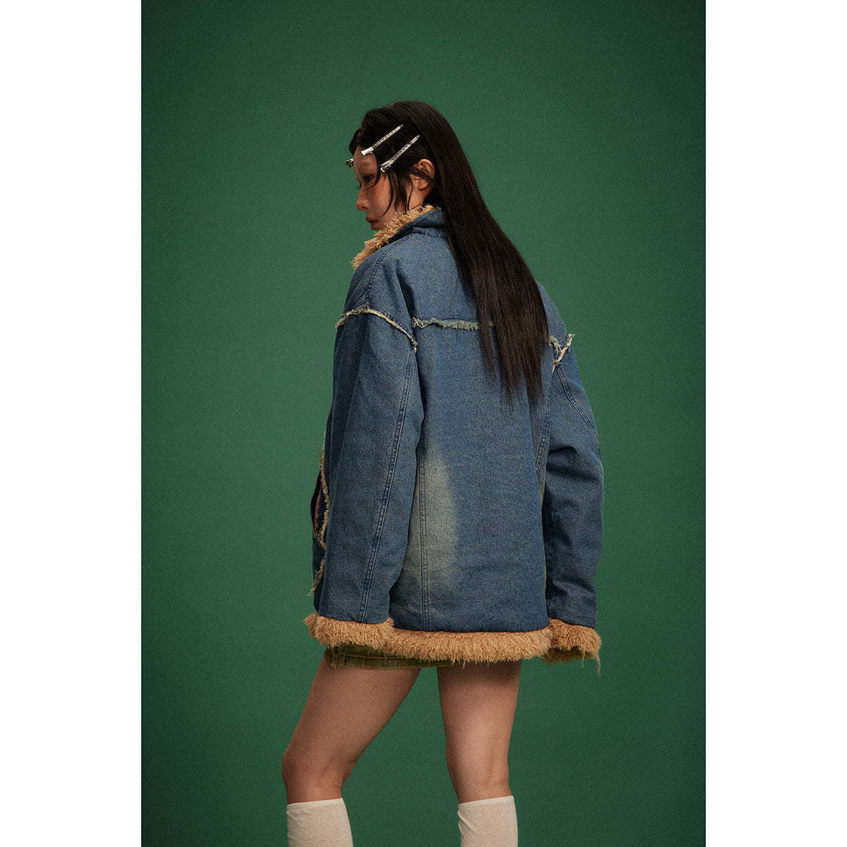Rear view of a model wearing a blue denim jacket with tan shaggy trim at the cuffs and hem.
