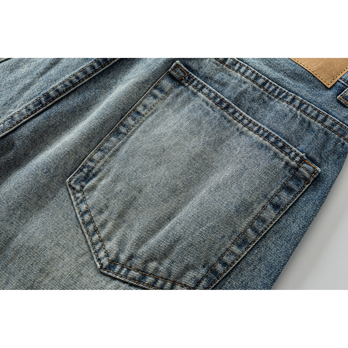 Close-up of faded blue jeans showing a rear pocket, contrast stitching, and a plain tan waistband patch.