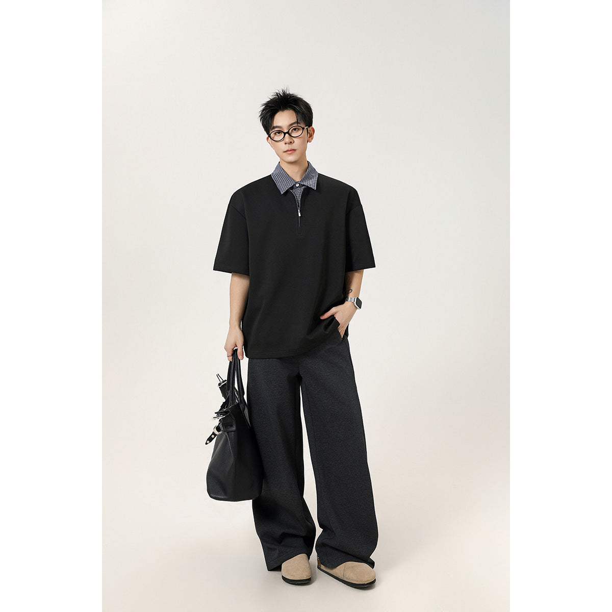 Model wearing a black short-sleeve quarter-zip polo with a checked collar and charcoal wide-leg trousers.