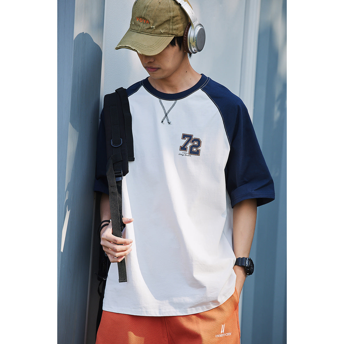 Model wearing a white T-shirt with navy raglan sleeves and a chest number graphic, shown from the front.