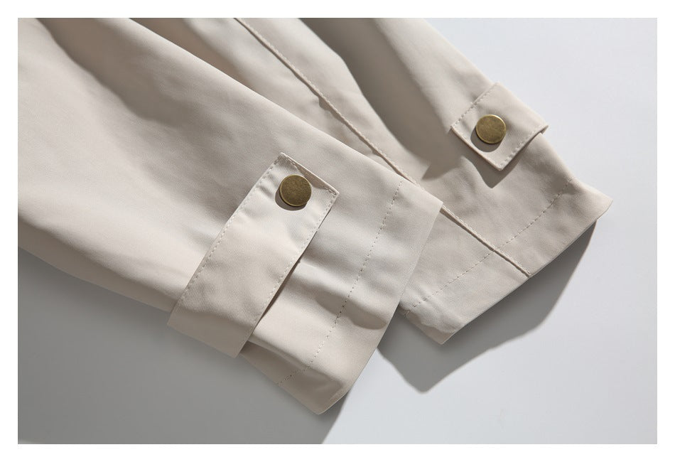 Close-up of a light beige jacket's sleeve cuffs with brass-tone snap buttons.
