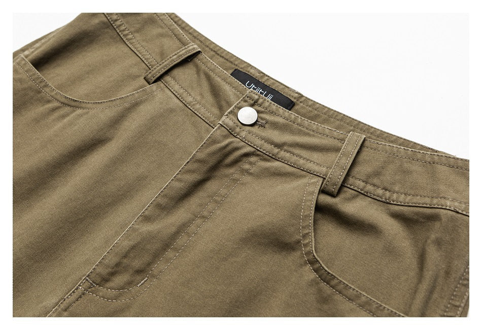 Close-up of brown trousers at the front waist, with a button, belt loop, and curved pockets.