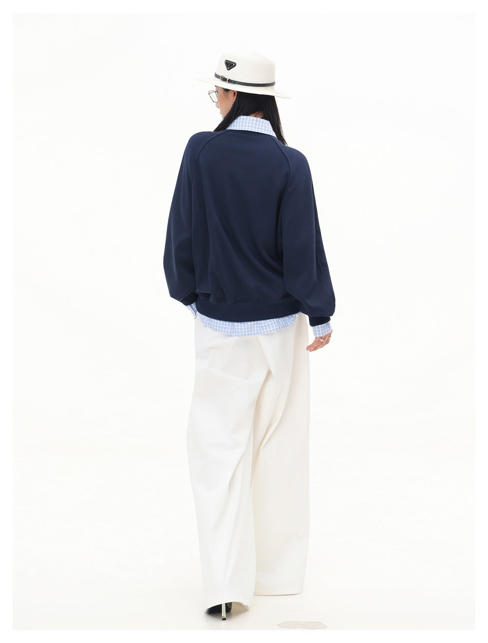 Rear view of a model wearing a navy sweatshirt with a blue checked shirt peeking out at the collar, cuffs, and hem.