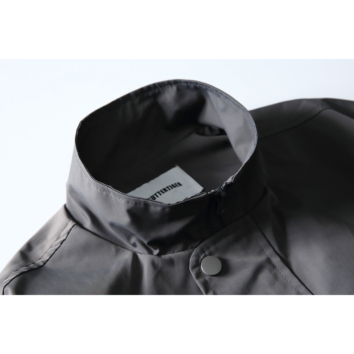 Close-up of a charcoal jacket's stand collar, zipper, snap closure, and inner neck label.