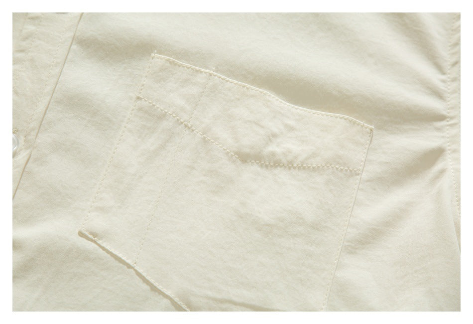 Close-up of an ivory garment’s stitched patch pocket and curved top seam.