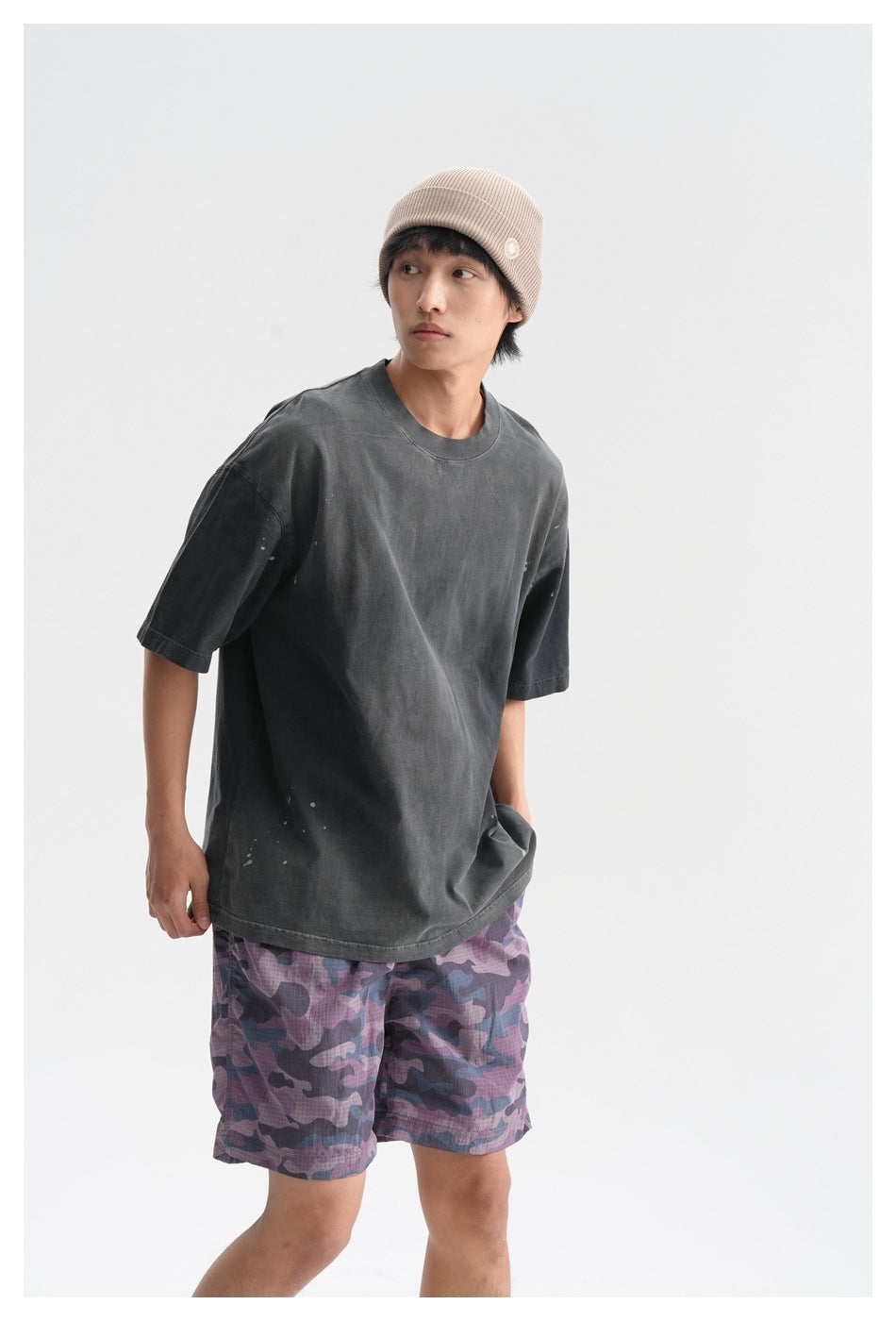 Three-quarter mid-length view of a model wearing a charcoal T-shirt and purple camouflage shorts.