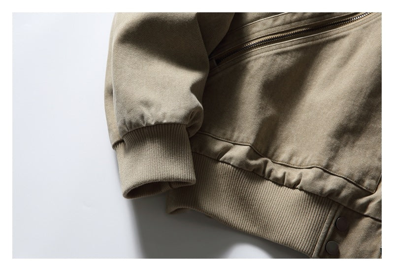 Close-up of the taupe jacket's ribbed cuff and hem with a diagonal zip pocket and snap buttons.