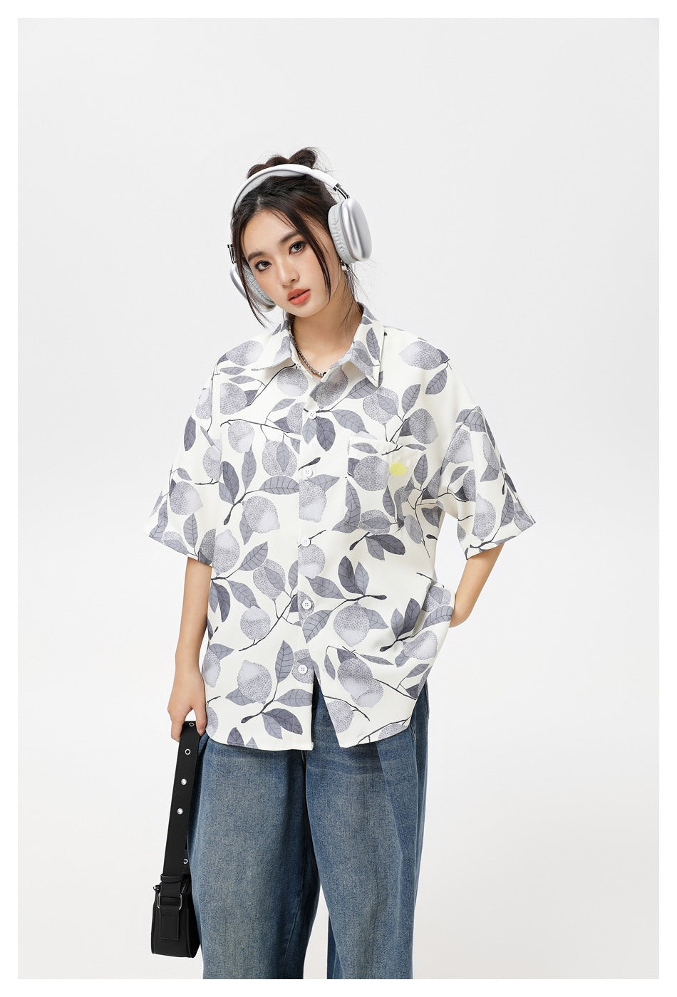 Model wearing a loose ivory short-sleeve button-up shirt with a gray lemon-and-leaf print and blue jeans.