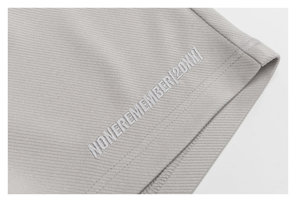 Close-up of white embroidered lettering near the hem of light gray shorts.
