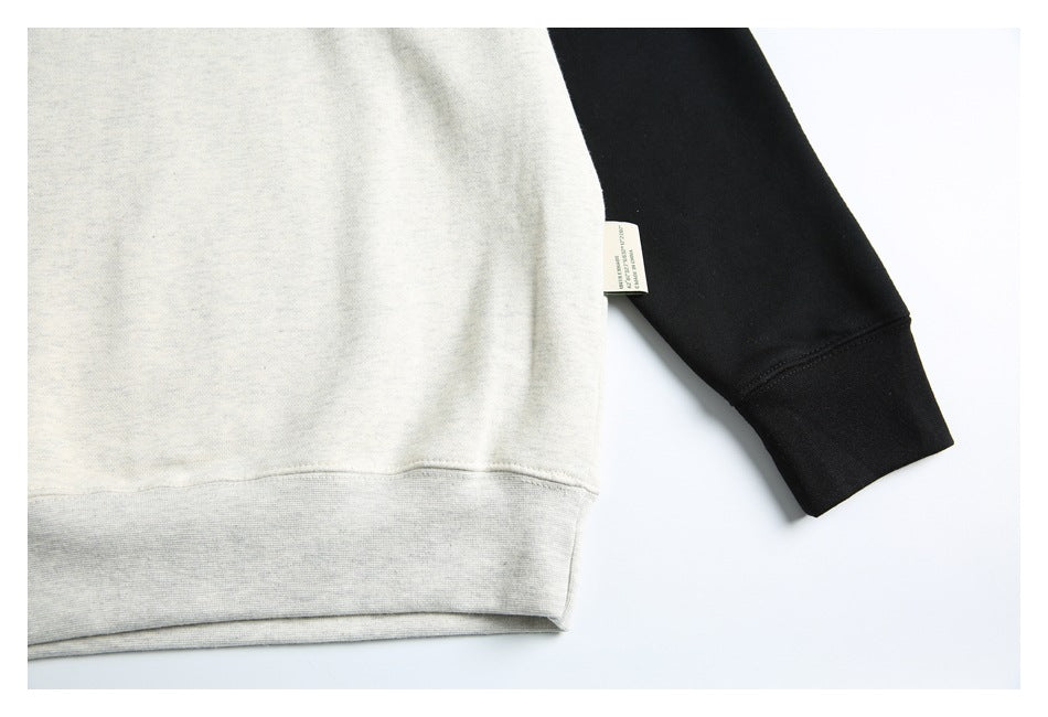 Close-up of the off-white sweatshirt hem and black sleeve cuff, with a small side-seam label.