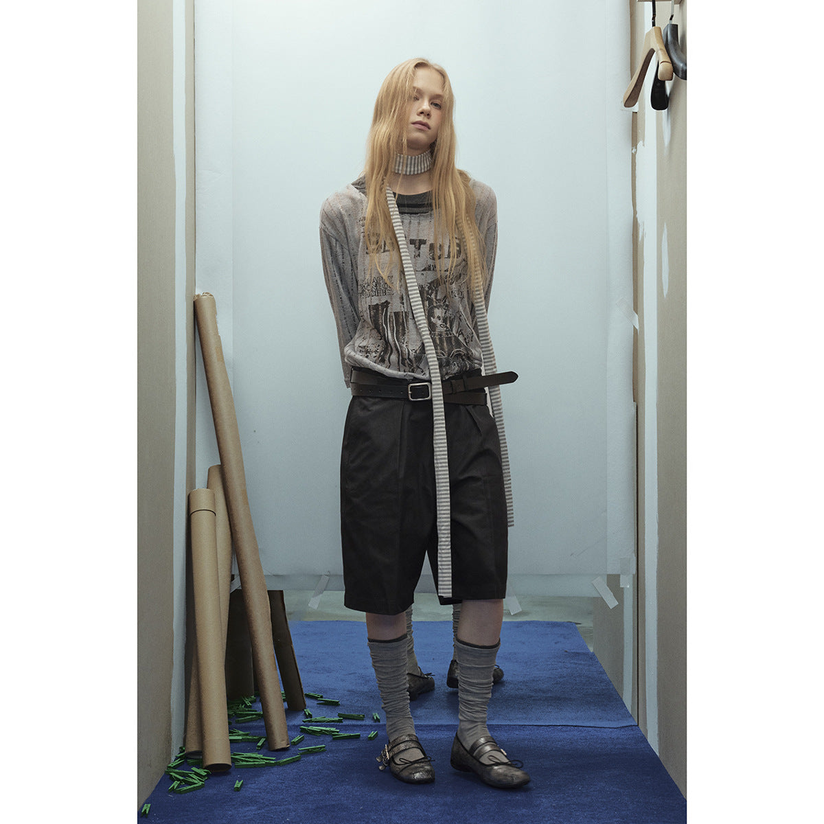 Front view of a model wearing a gray graphic top, long striped scarf, and black knee-length shorts.