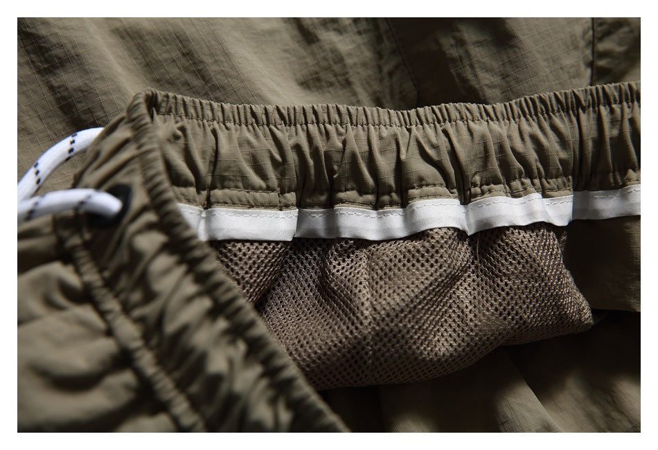 Close-up inside olive-khaki shorts showing the elastic waistband, white trim, drawcord, and mesh lining.