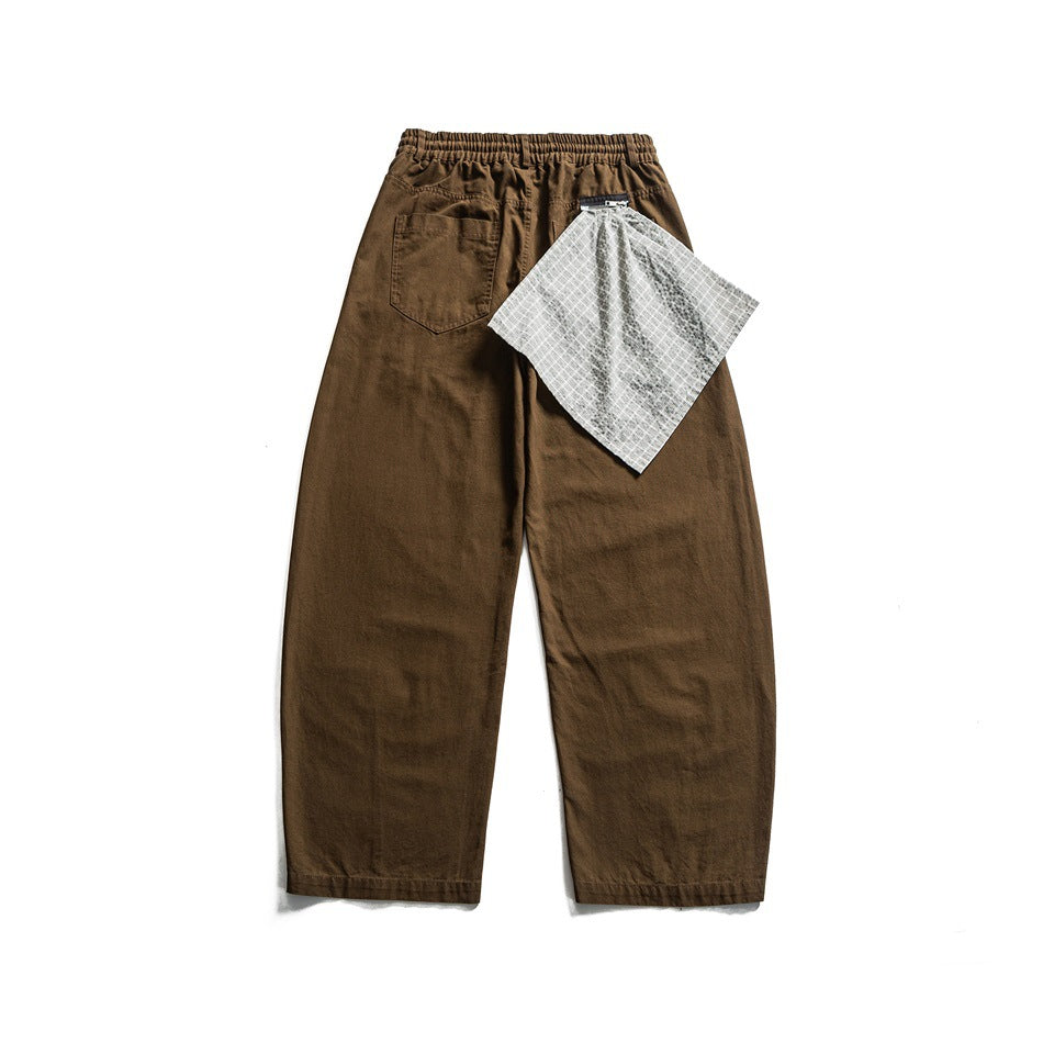 Back view of brown wide-leg pants with elastic waistband, patch pocket and gray checked cloth hanging at the waist