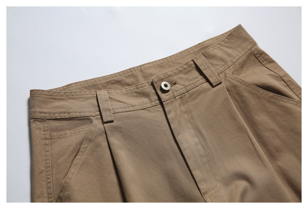 Close-up of tan trousers at the front waistband, showing the button, belt loops, fly, and angled pocket.