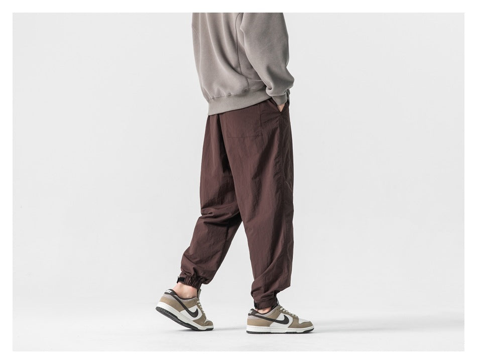 Model wearing dark brown loose-fit jogger pants with elastic cuffs, shown from the back and side.
