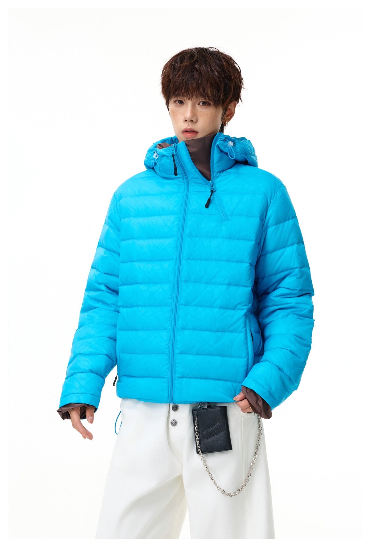 Front view of a model in a bright cyan quilted hooded jacket, worn open at the collar with white trousers.