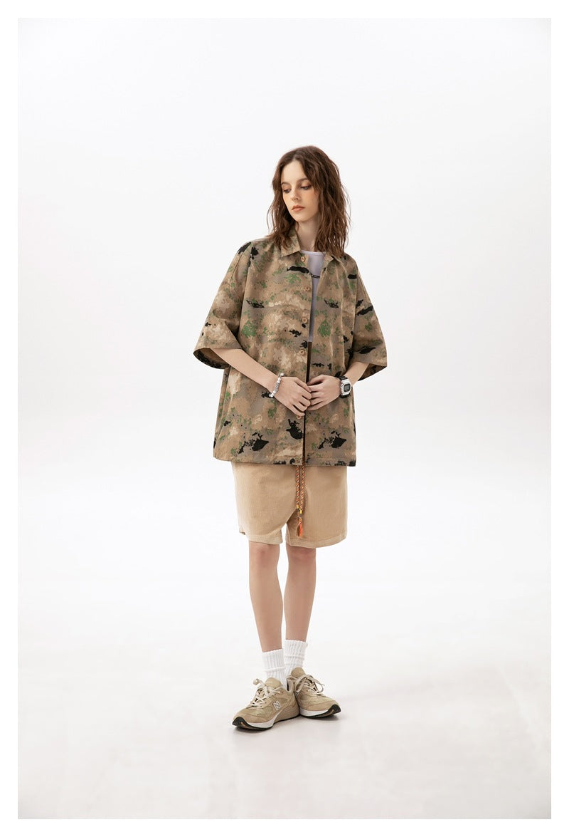 Model wearing a short-sleeved camouflage button-up shirt and light tan shorts against a white studio background.