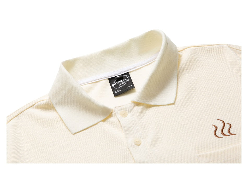 Close-up of an ivory polo shirt's collar, buttons, chest pocket, and small brown embroidered motif.