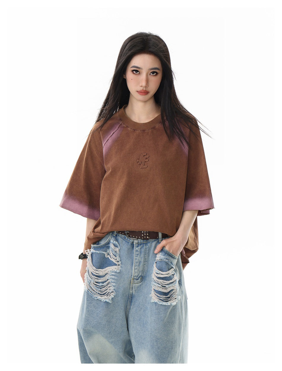 Model wearing an oversized brown short-sleeve shirt with mauve faded accents and a small raised chest emblem.