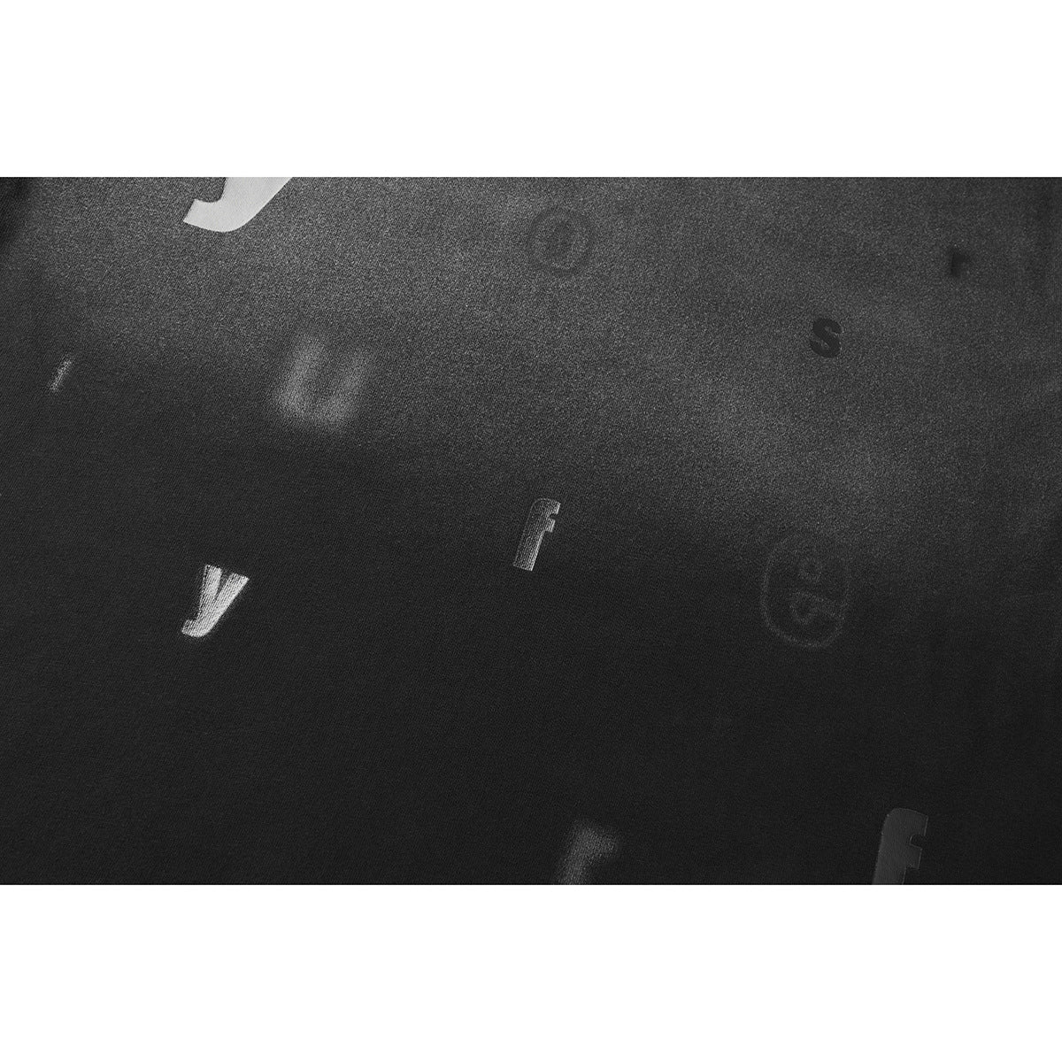 Close-up of dark T-shirt fabric with scattered faint letters and a few lighter letter shapes.
