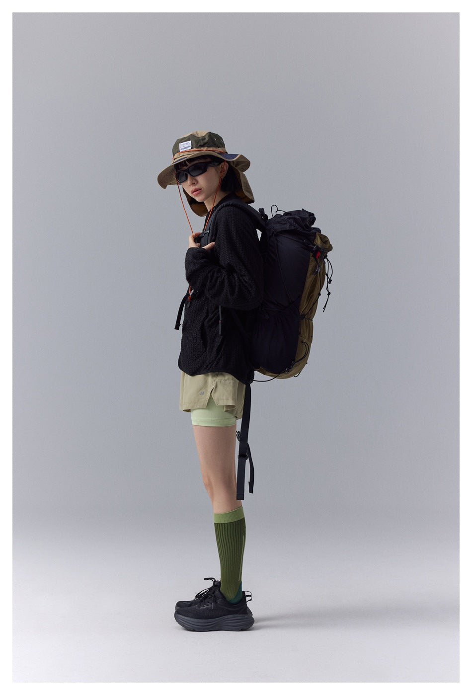 Side view of a model wearing a black textured jacket with a hiking backpack.