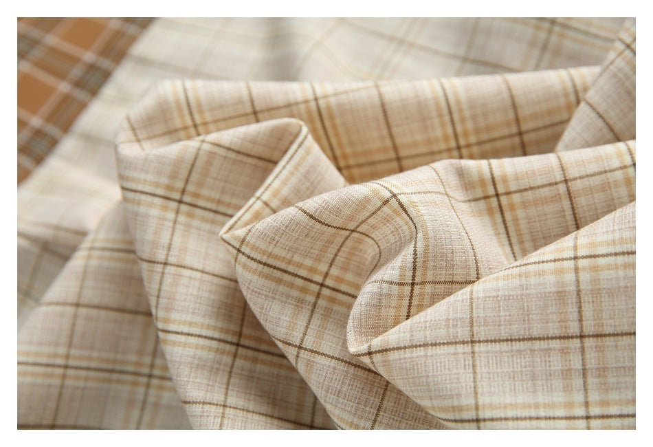 Close-up of folded cream plaid shirt fabric with brown intersecting lines.