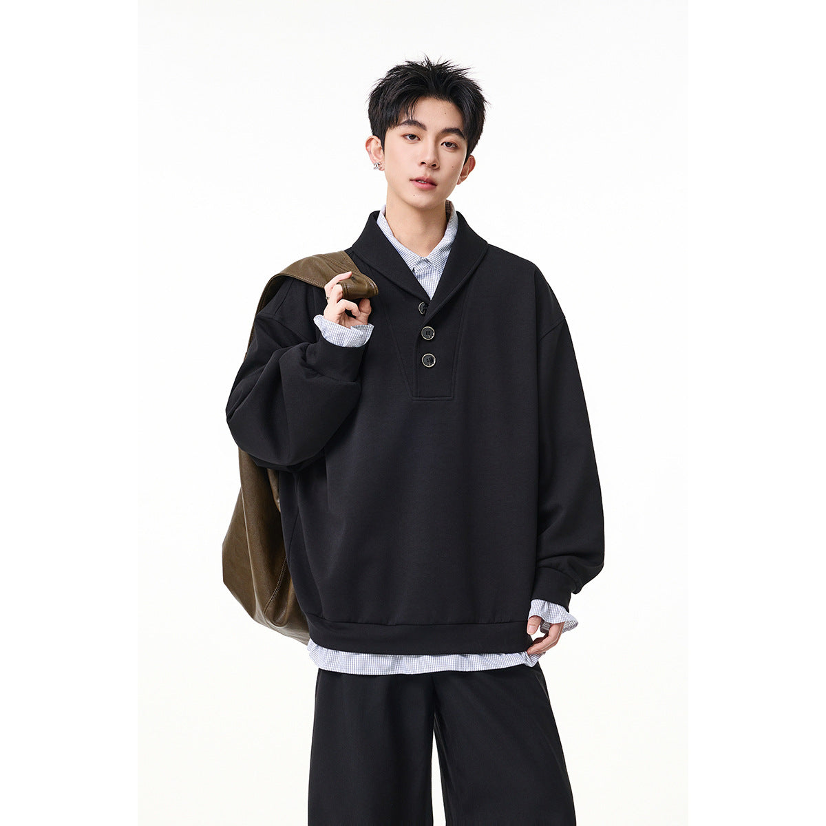 Model wearing a black oversized shawl-collar pullover over a pale blue shirt, with a brown bag over one shoulder.
