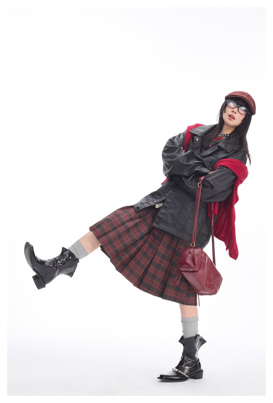 Model posing in a charcoal jacket, red-and-black plaid skirt, red knit layer, and black boots.