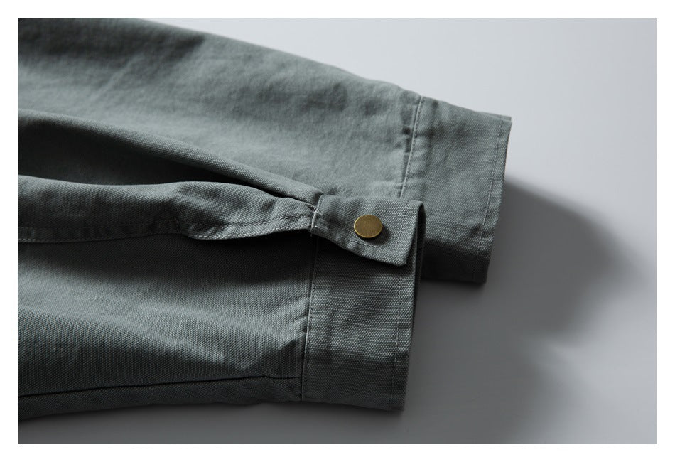 Close-up of a gray-green sleeve cuff with a tab and round brass-colored snap.
