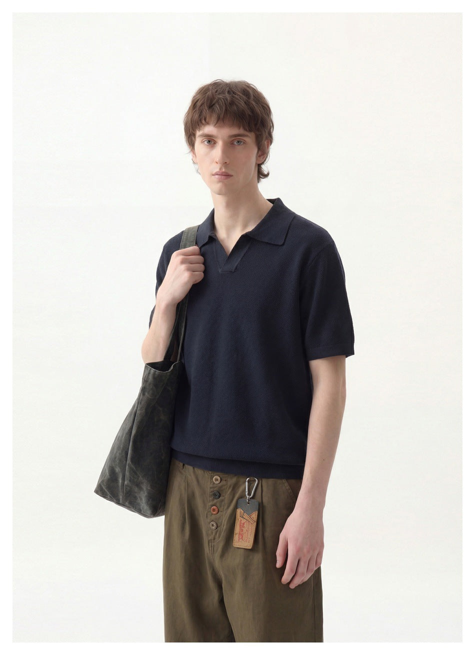 Man wearing a navy knit polo with open collar, carrying a gray tote bag, with olive trousers