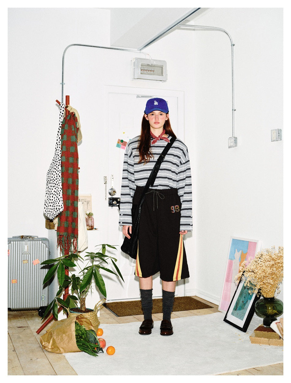 Front view of a model wearing a gray-and-black striped long-sleeve top and black shorts with red and yellow side stripes.
