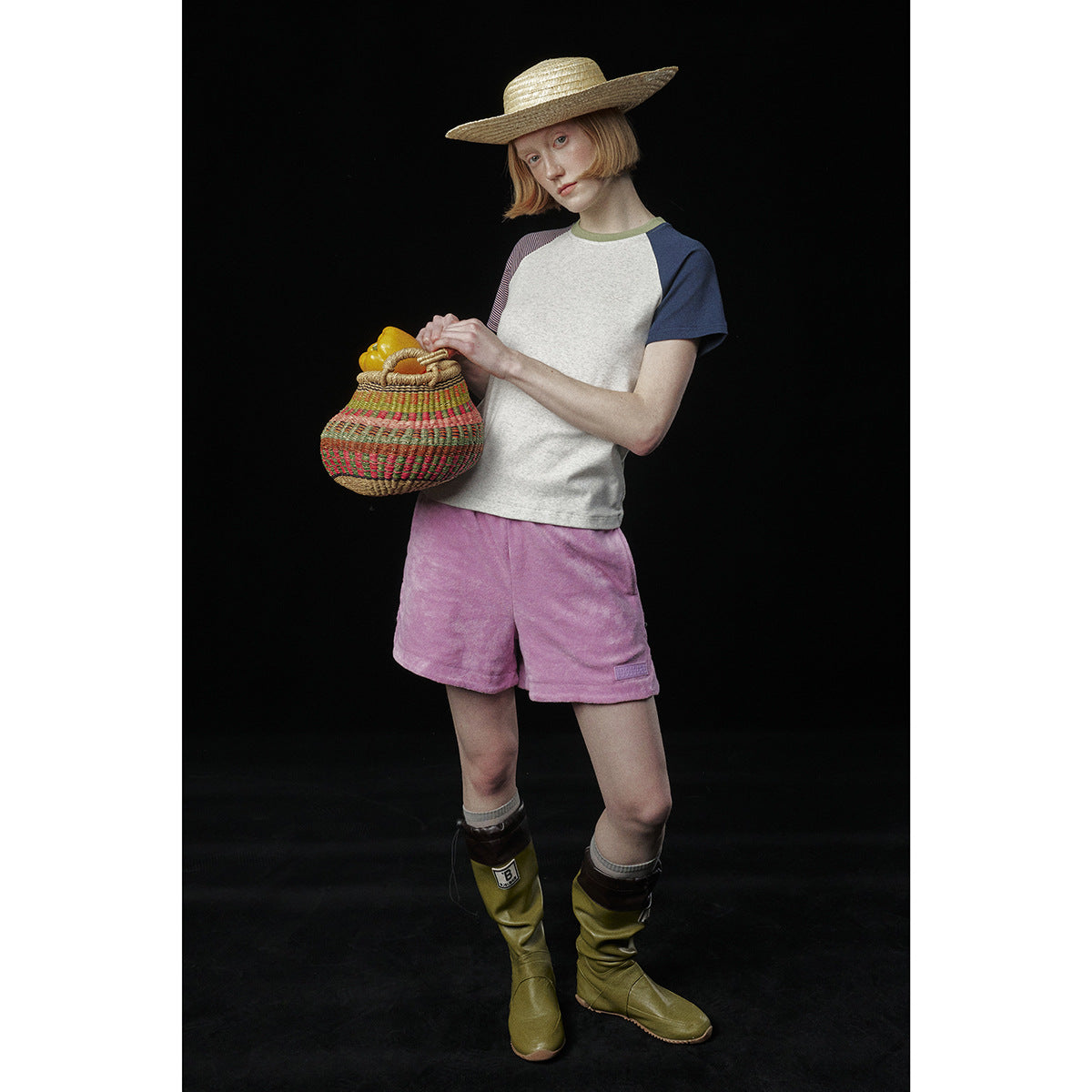Model wearing an off-white raglan T-shirt with navy and striped sleeves, pink shorts, and a straw hat.