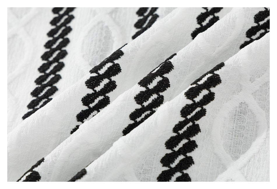 Close-up of folded white textured fabric with repeated black embroidered bands.