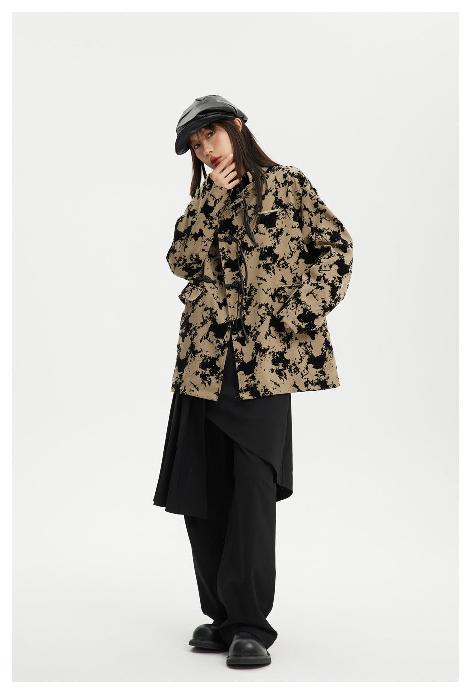 Model in khaki mottled-print jacket with frog closures and flap pockets, styled with black layered skirt, pants and cap