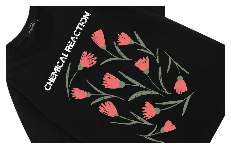 Close-up of a black T-shirt with coral flowers, muted green stems, and white text printed on the front.