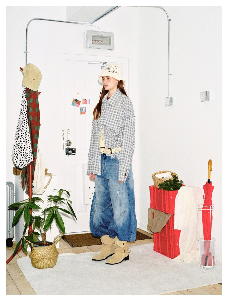 Side view of model in an oversized plaid shirt with wide-leg jeans, bucket hat and suede boots in a styled room