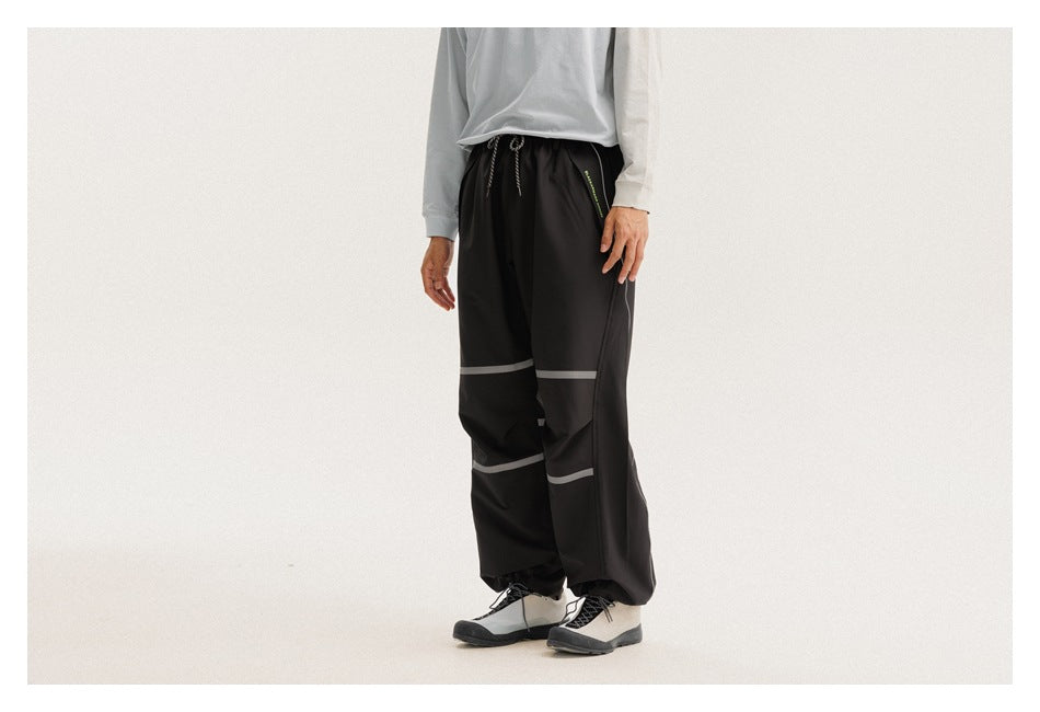 Angled front view of a model wearing loose black pants with gray leg bands and a zip pocket.