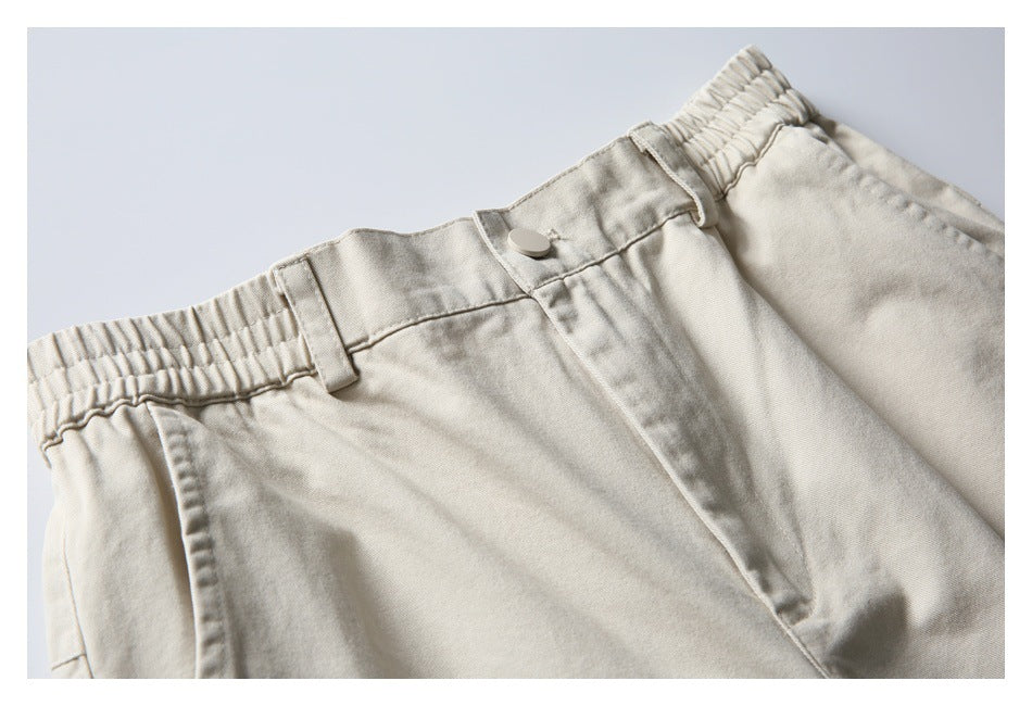 Close-up of light beige trousers showing an elastic waistband, belt loops, button, and front fly.