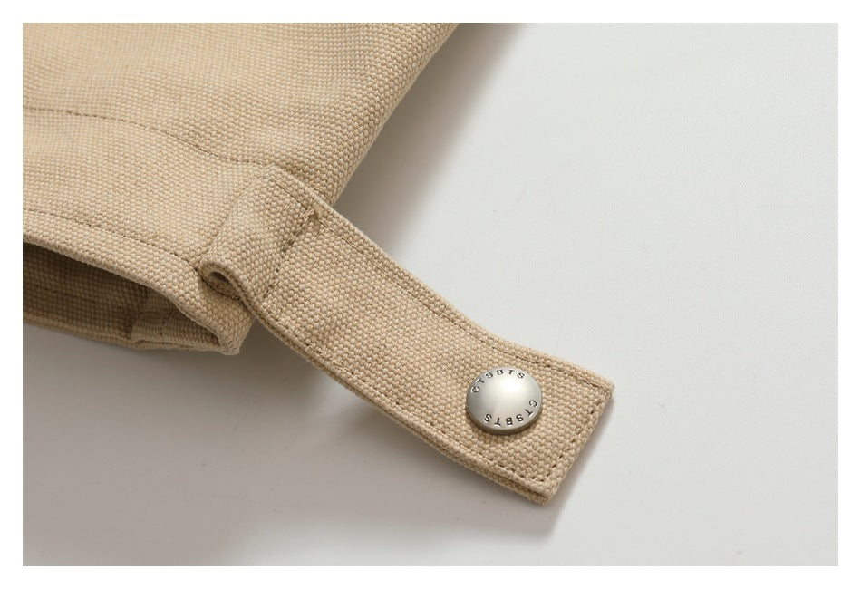 Close-up of a beige garment tab with a round metal snap engraved with letters.