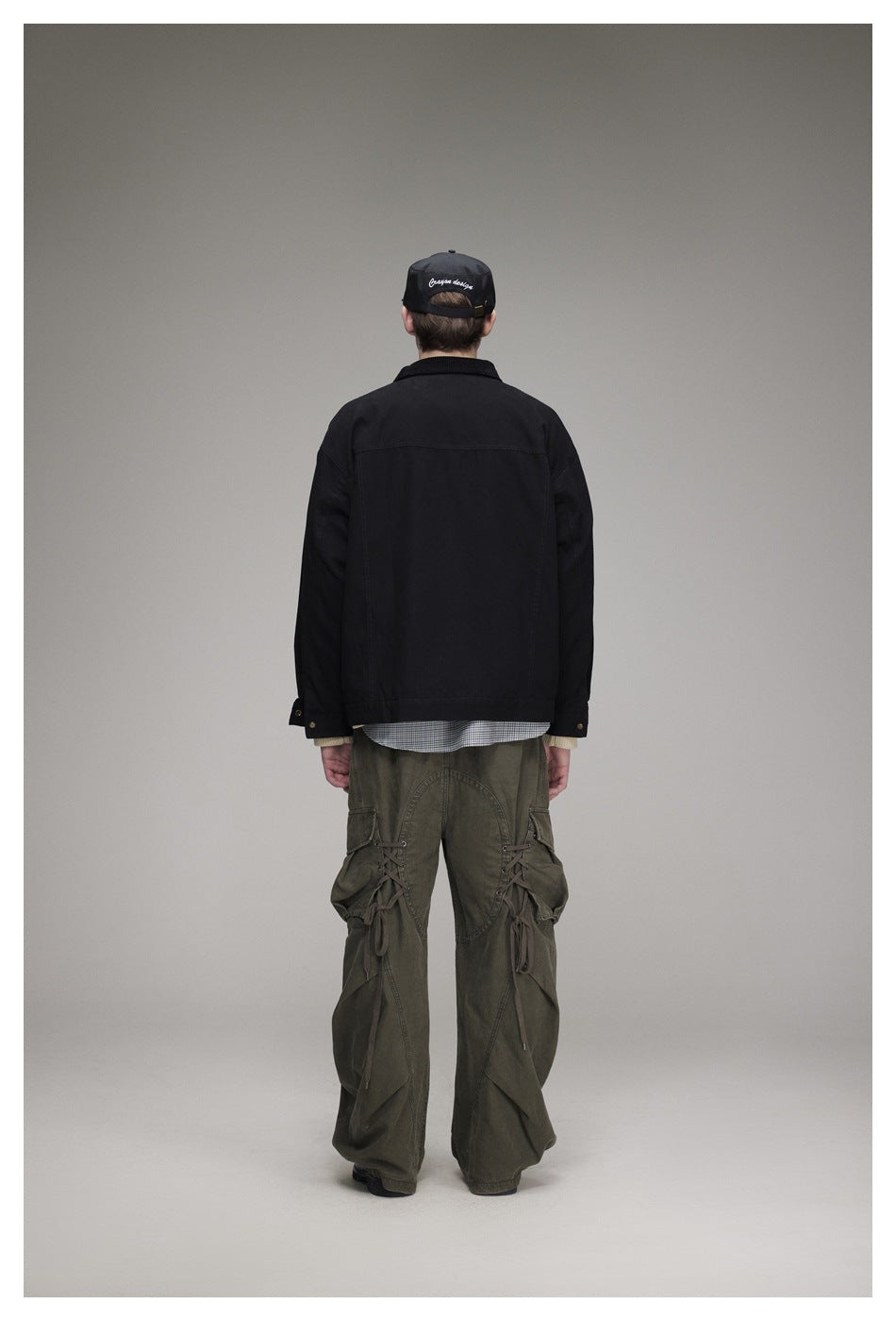 Rear view of a model wearing a black jacket and loose olive cargo pants with lace-up leg details.