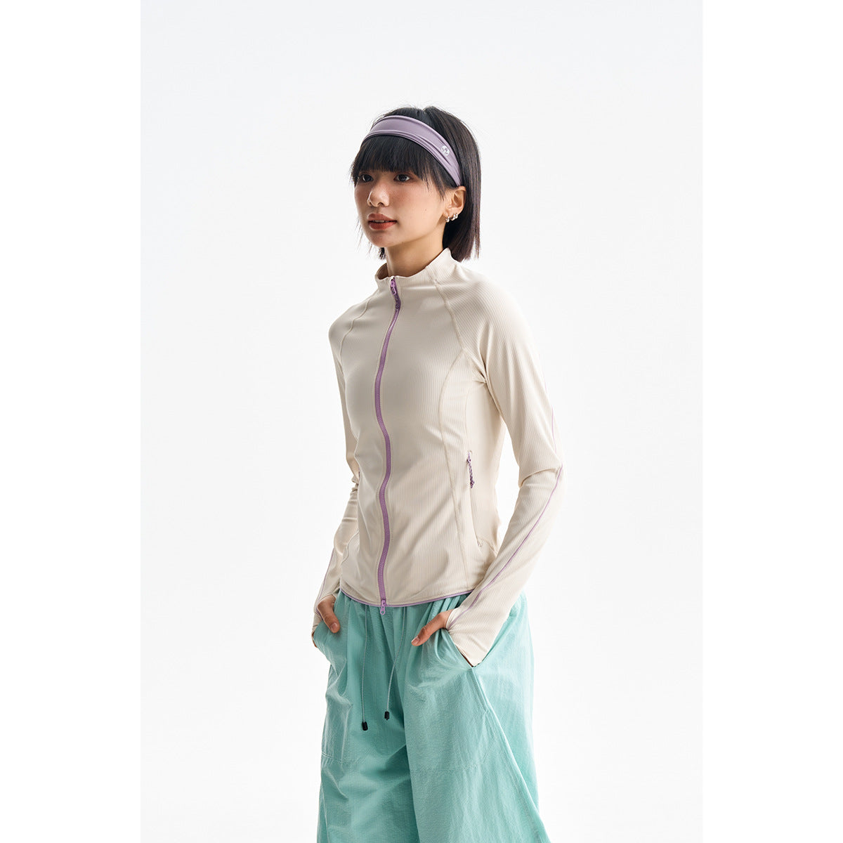 Model wearing an ivory zip-front jacket with lilac trim and loose aqua trousers, shown from head to mid-leg.