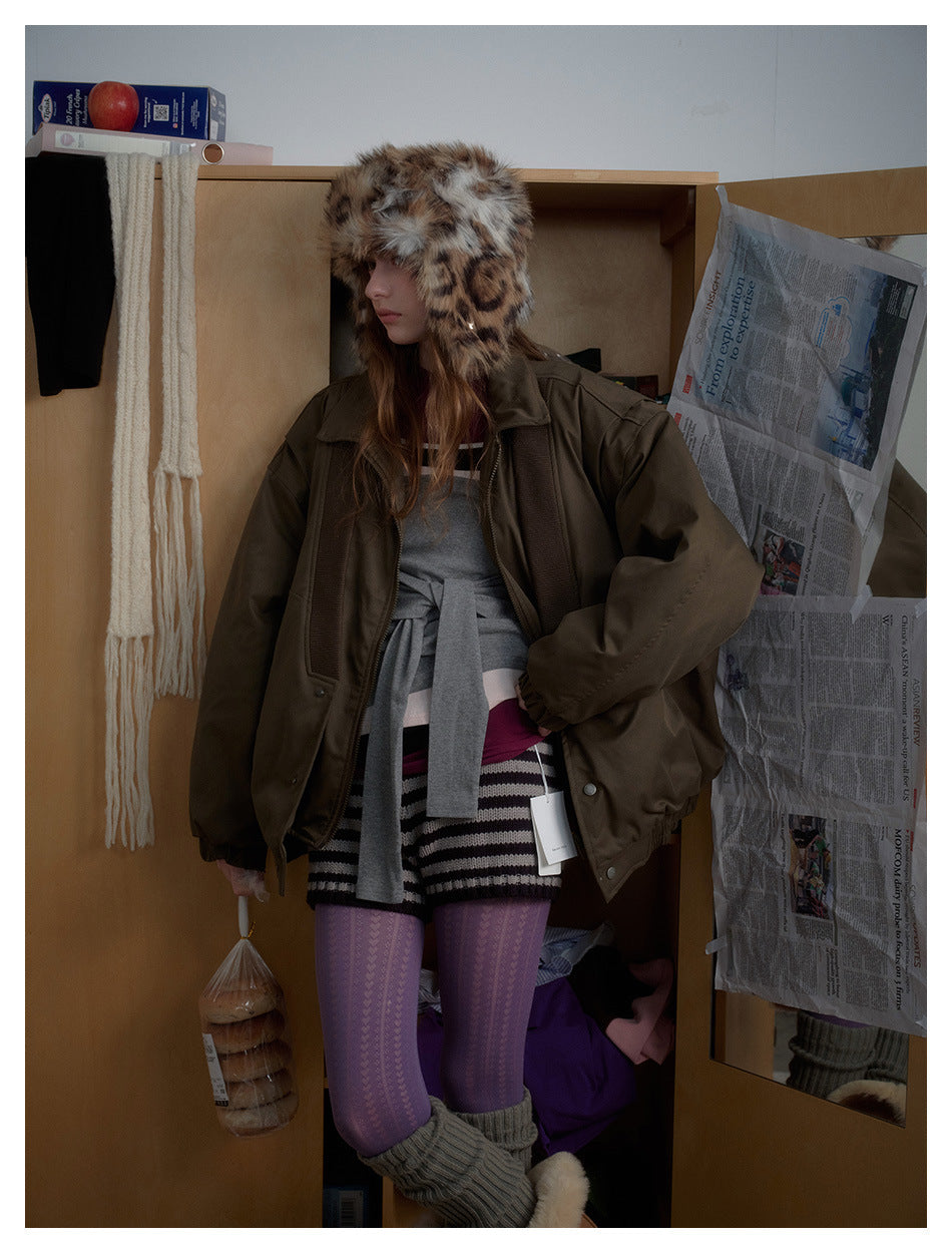 Model in a roomy olive-brown jacket with ribbed front panels, shown at an angle with a spotted faux-fur hat.