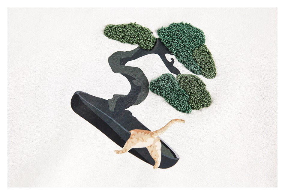Close-up of a raised green-textured tree and tan cat graphic on ivory fabric.
