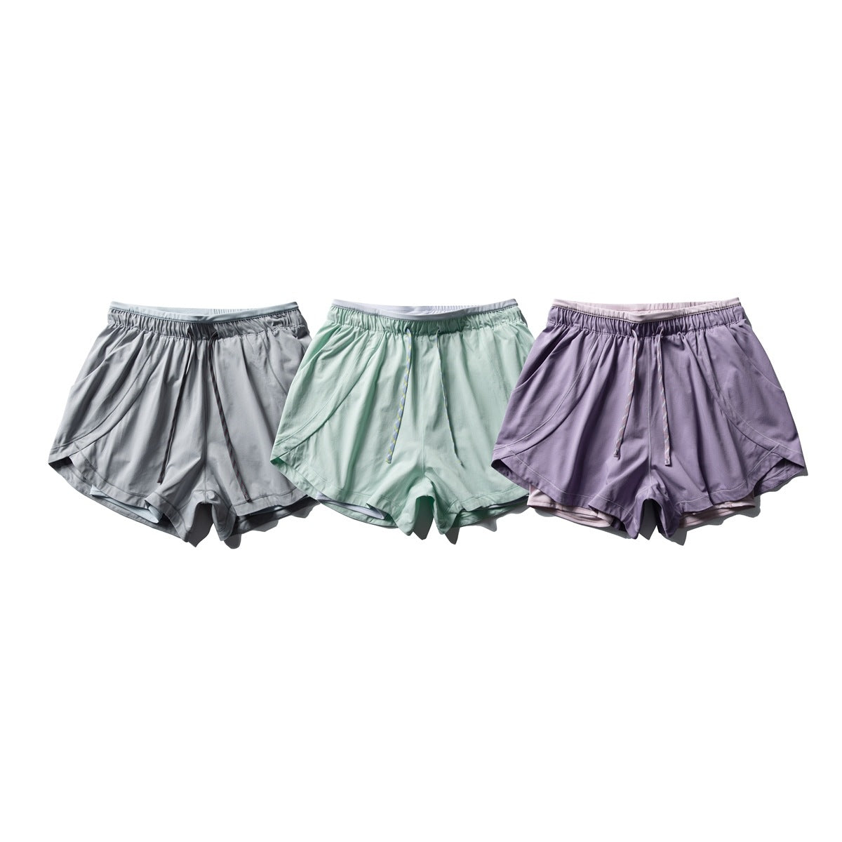 Three pairs of loose drawstring athletic shorts shown together in gray, mint green, and lavender.
