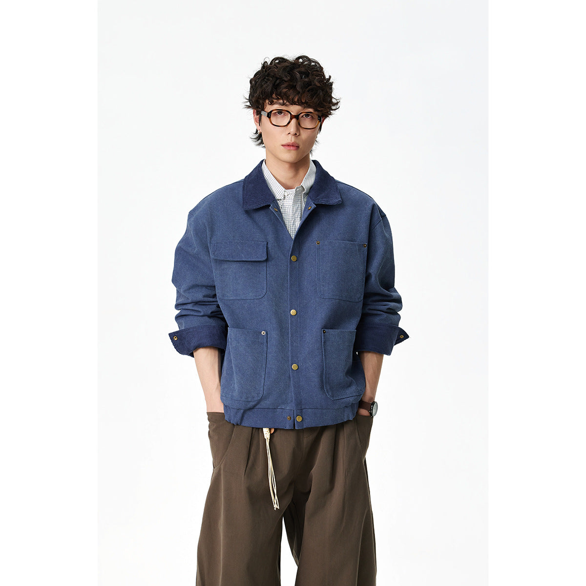 Model wearing a blue four-pocket work jacket over a checked shirt and wide brown trousers.