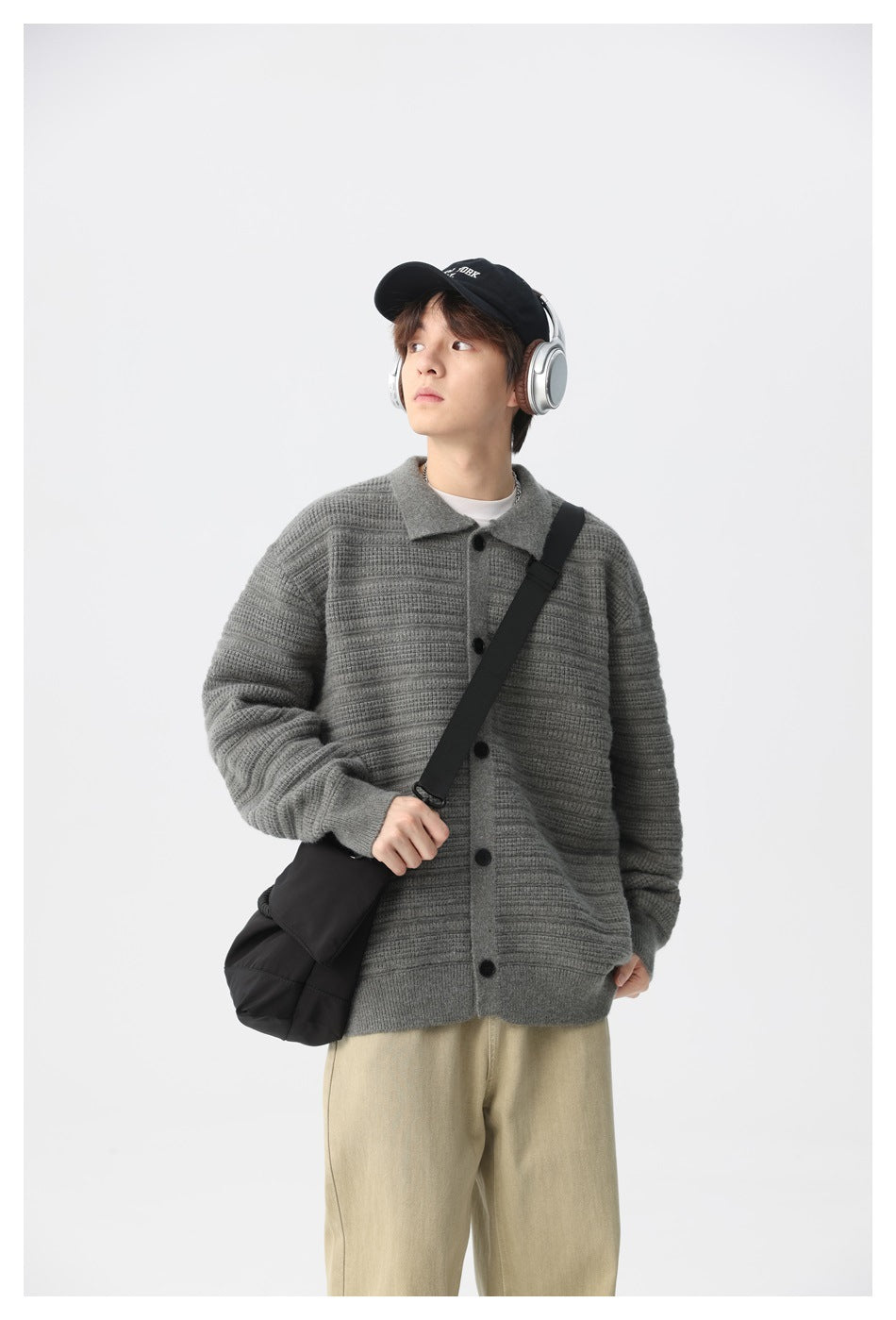 Model wearing a gray textured knit cardigan with a collar and black buttons, carrying a black bag and wearing headphones.