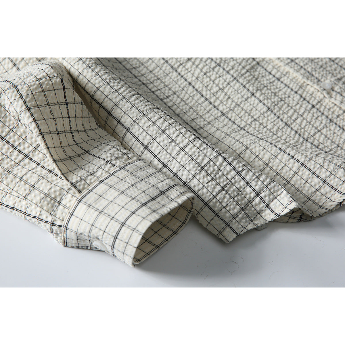 Close-up of the cream-and-black checked shirt fabric, front placket, and buttoned sleeve cuff.