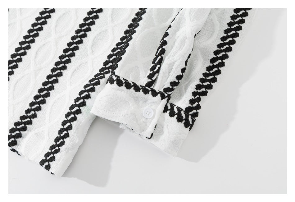 Close-up of a white cuff with a button and black embroidered stripes on the garment.