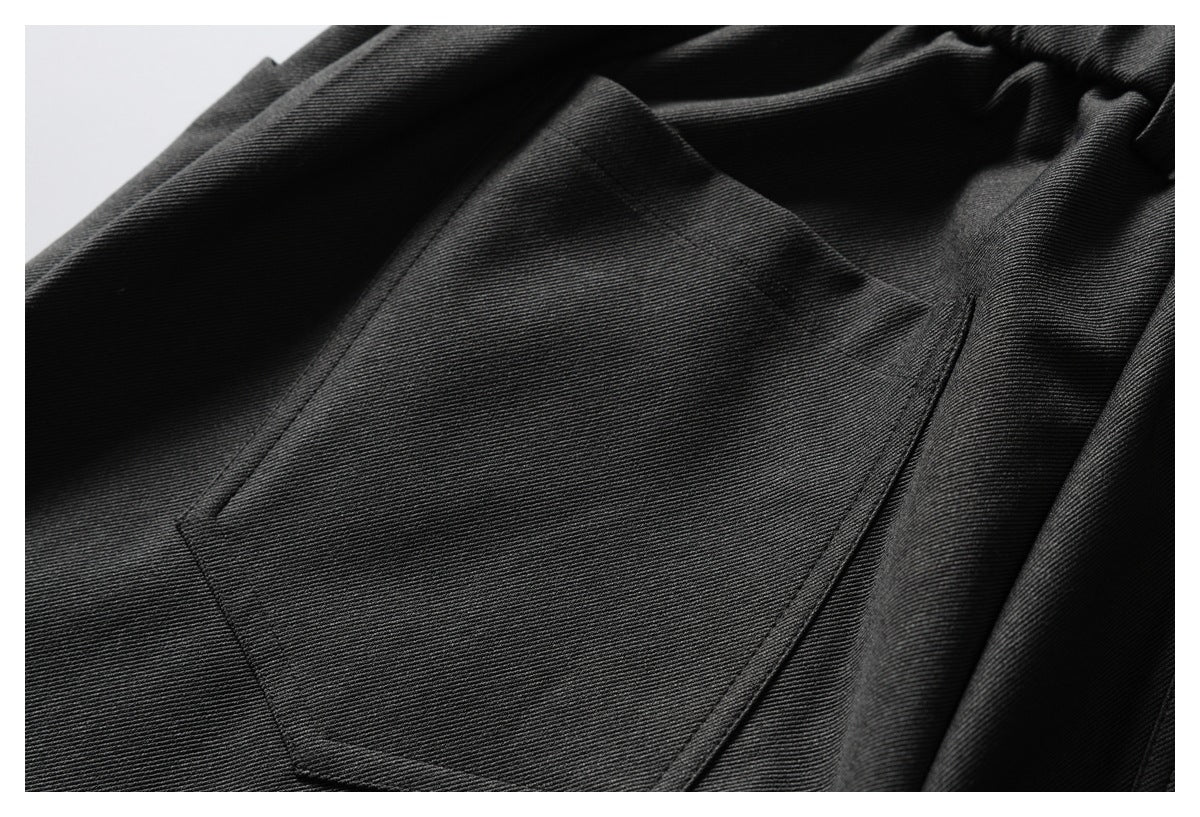 Close-up of a large patch pocket on dark trousers, highlighting the stitching and woven texture.